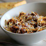 bowl of beer chili spaghetti topped with cheese and diced red onion