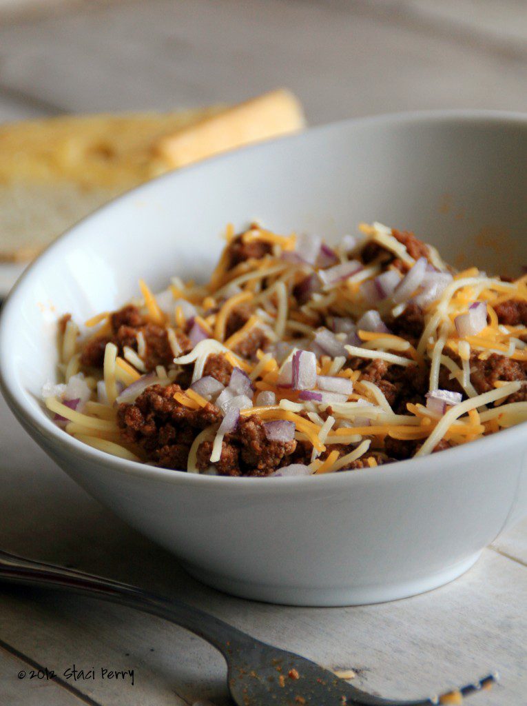 bowl of beer chili spaghetti topped with cheese and diced red onion 