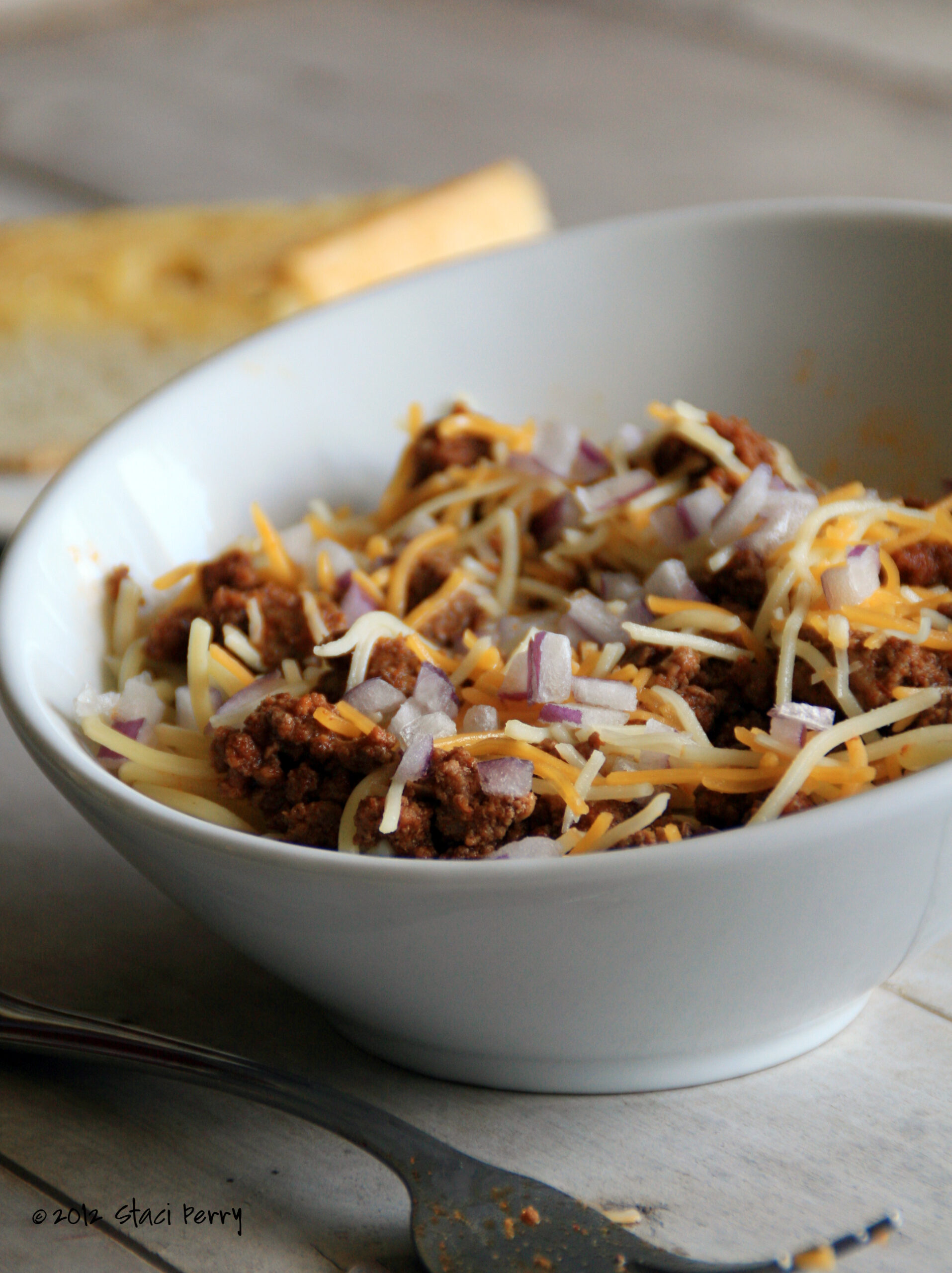 bowl of beer chili spaghetti topped with cheese and diced red onion