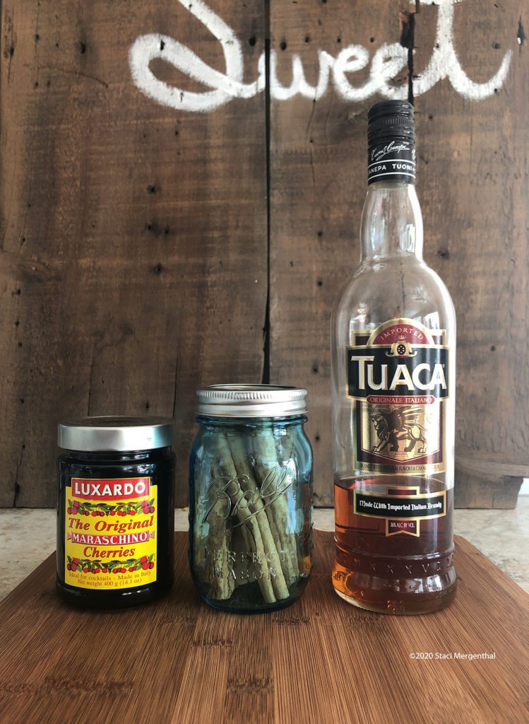 Luxardo cherries mason jar of cinnamon sticks and a bottle of Tuaca