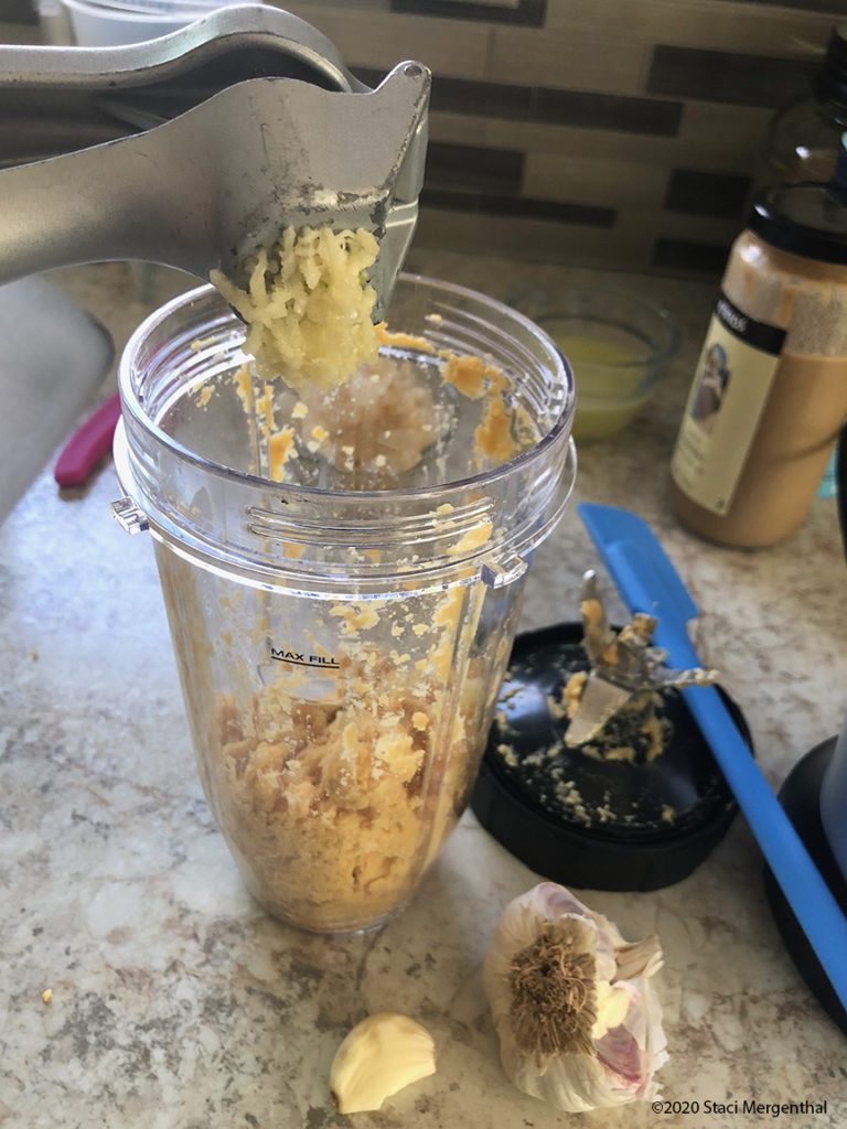 using a garlic press to add garlic to chickpeas in Ninja container