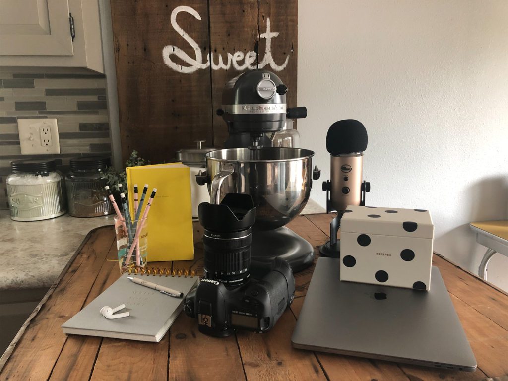 podcast microphone, laptop, recipe box, Kitchenaid stand mixer, journal, AirPods, camera, pencils 