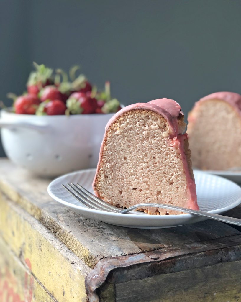 piece of strawberry pound Bundt cake on plate with bowl of strawberries and second piece of cake in background 