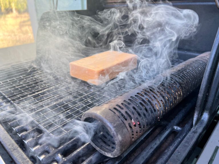 block of cheese on a grill with a smoking smoke tube