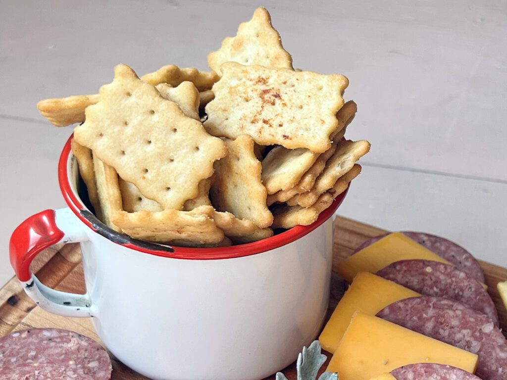 cup of smoked Chicken In A Biskit crackers on a tray with smoked cheese and summer sausage