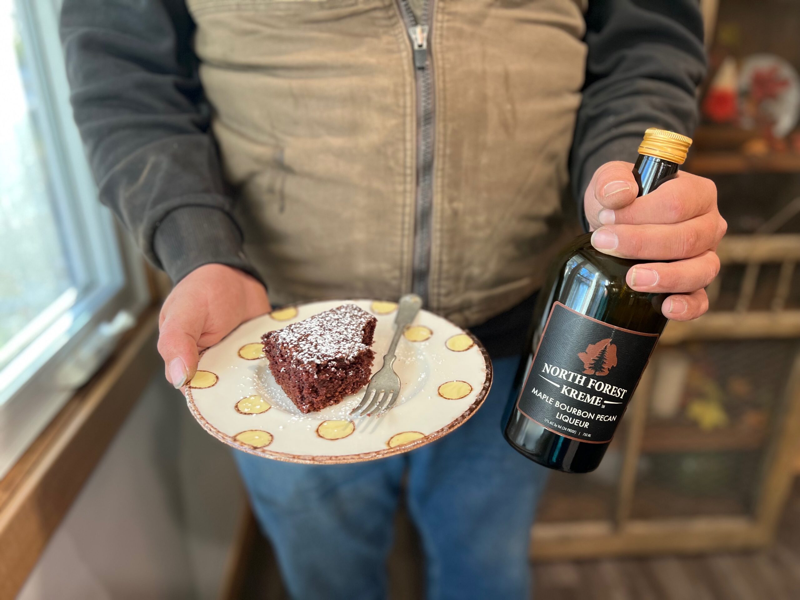 man holding plate of cake with alcohol and bottle of North Forest Maple Bourbon Pecan Kreme liqueur
