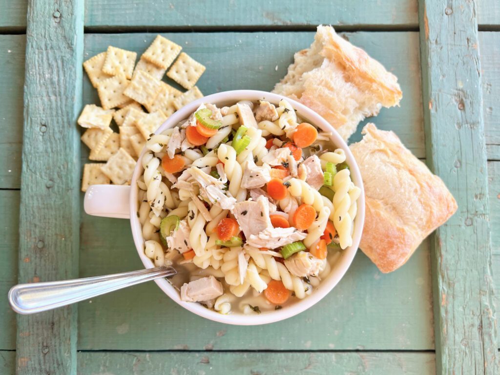 big mug full of turkey noodle soup with crackers and bread