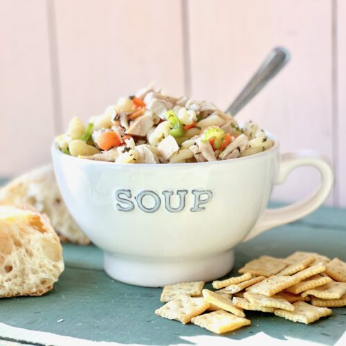 soup mug full of turkey noodle soup with bread and crackers