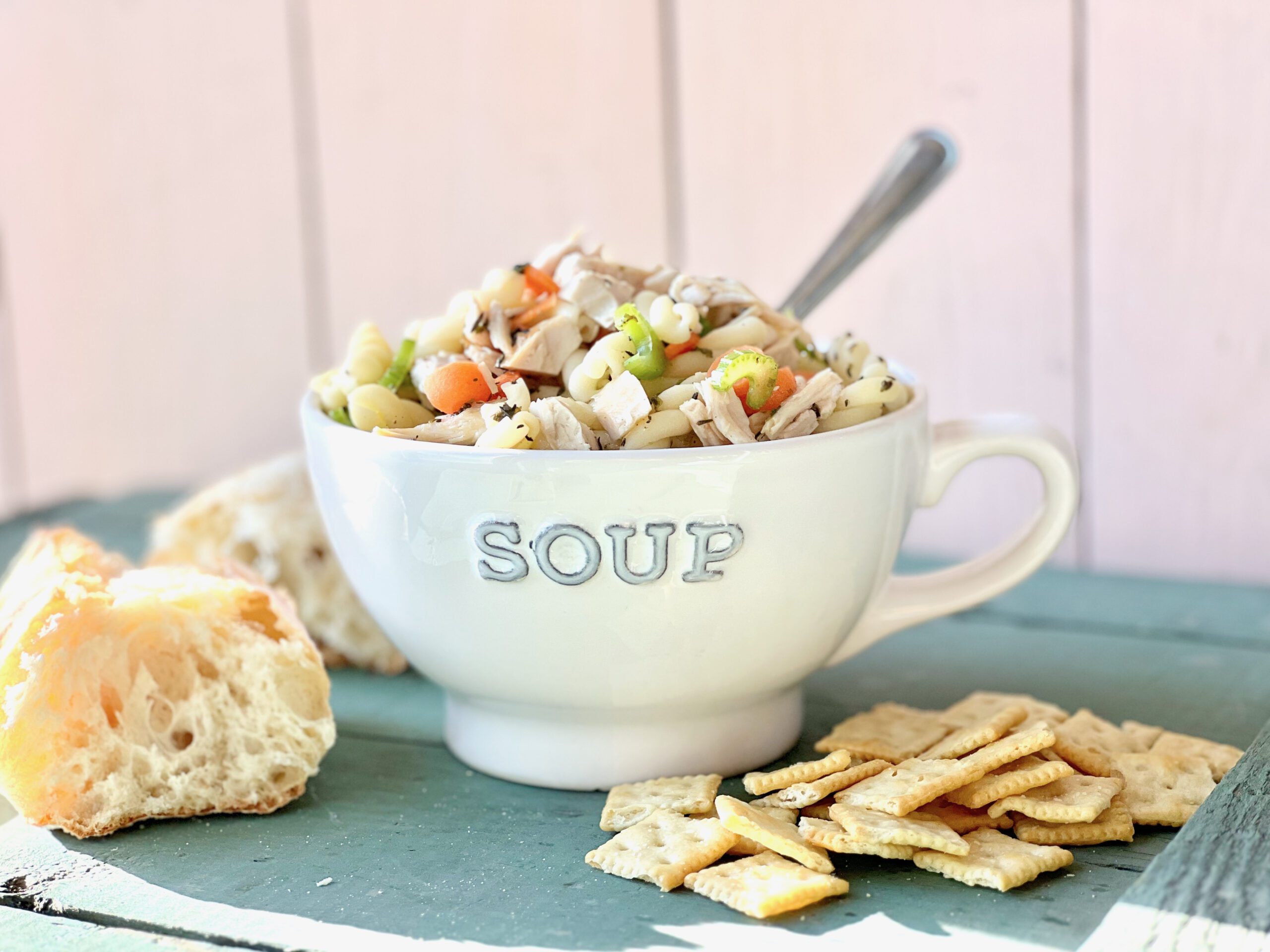 soup mug full of turkey noodle soup with bread and crackers