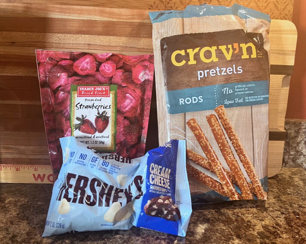 bag of pretzel sticks, HERSHEY's cream cheese chips, and Trader Joe's freeze-dried strawberries ingredients for deconstructed strawberry pretzel salad sticks
