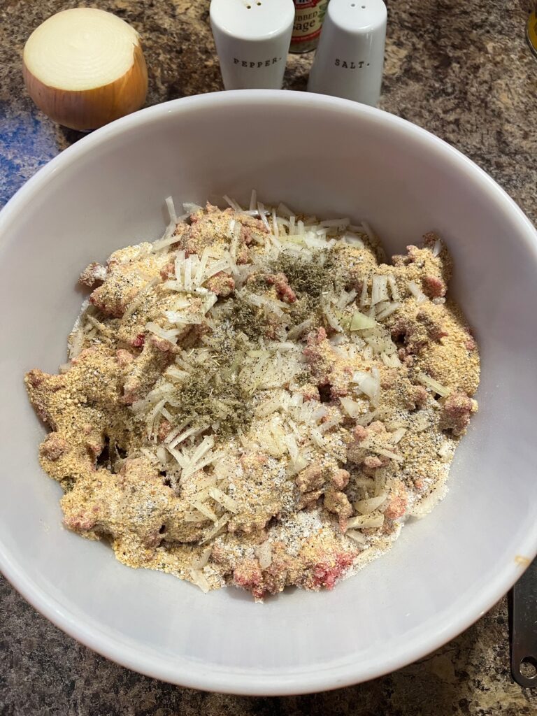 breadcrumbs, salt, pepper and sage added to meatloaf mixture in a bowl