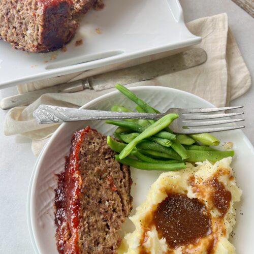 plate with mashed potatoes and gravy, a slice of meatloaf and green beans
