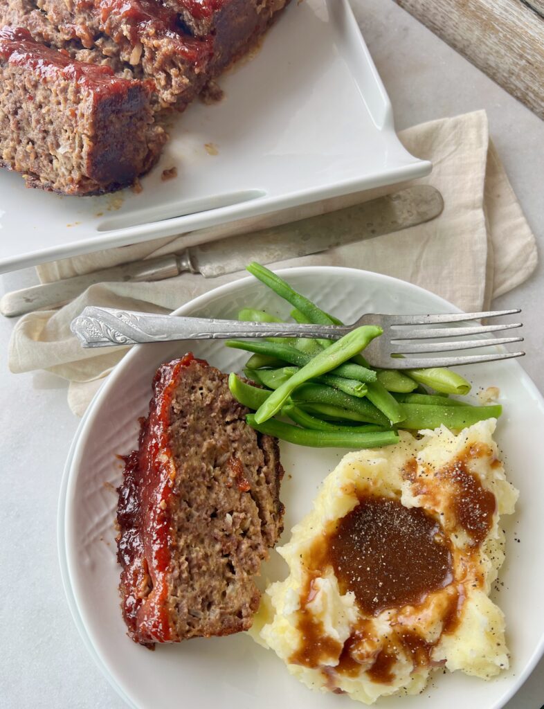 plate with mashed potatoes and gravy, a slice of meatloaf and green beans