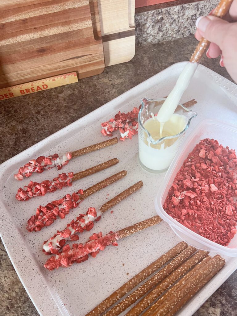 dipping pretzel rods into melted cream cheese chips for deconstructed strawberry pretzel salad sticks