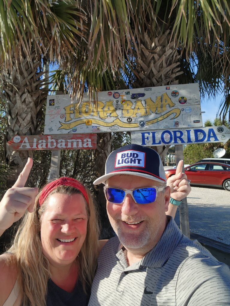 a man and a woman standing on the border between Florida and Alabama at Flora-Bama