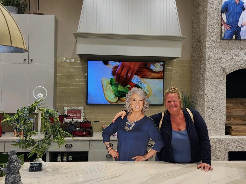 Staci standing next to a Paula Dean cardboard cutout at Paula Deen's Family Kitchen at OWA Foley Alabama 
