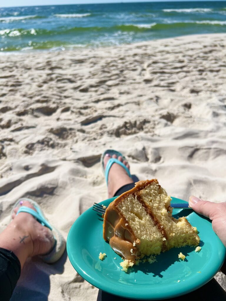 piece of caramel cake on a plate being held by someone on a Gulf Shores Alabama beach