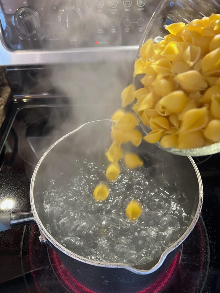adding pasta shells to pot of boiling water 
