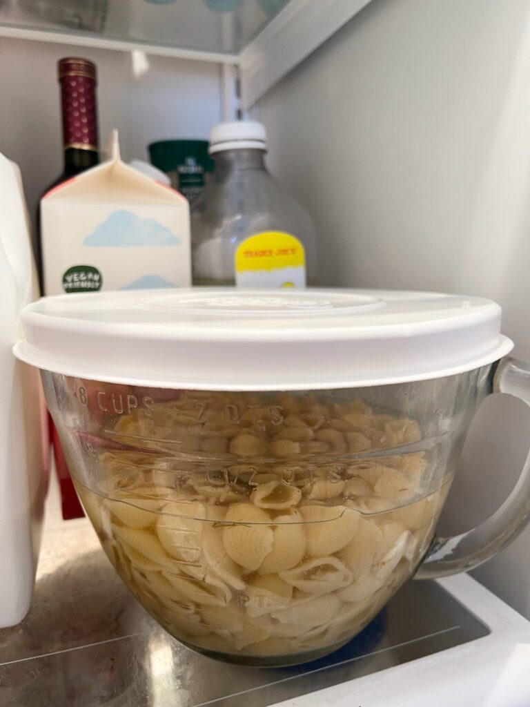 covered bowl of cooked pasta and pickle juice in refrigerator