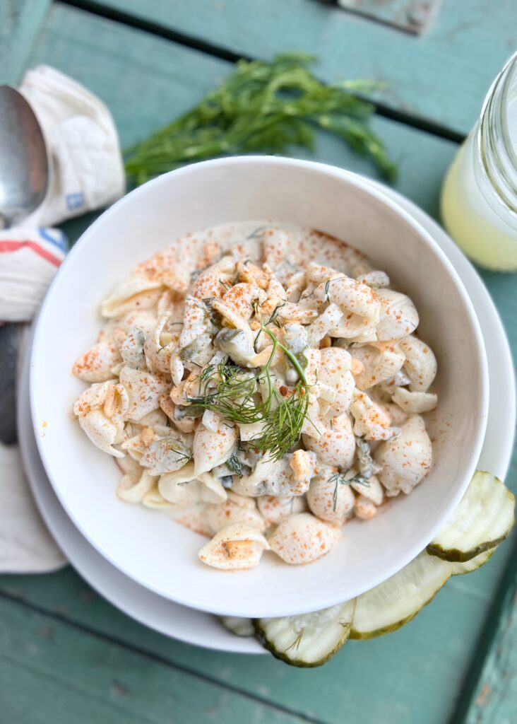 bowl with dill pickle pasta salad and a glass of lemonade and a spoon