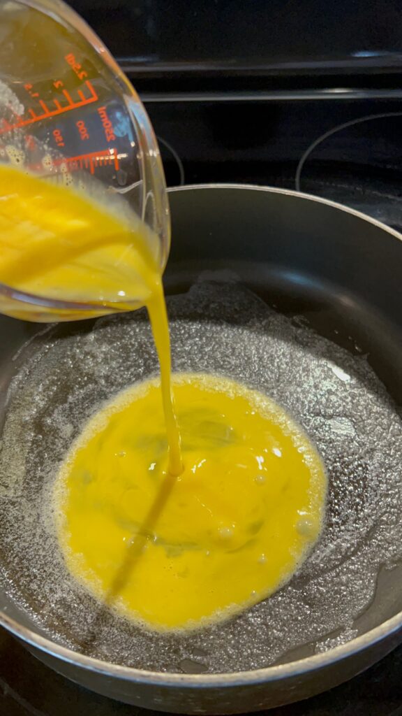 pouring two whisked eggs into a hot pan of melted butter