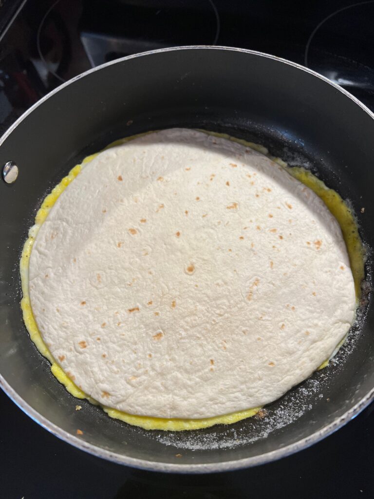 tortilla laying on top of two scrambled eggs in a pan