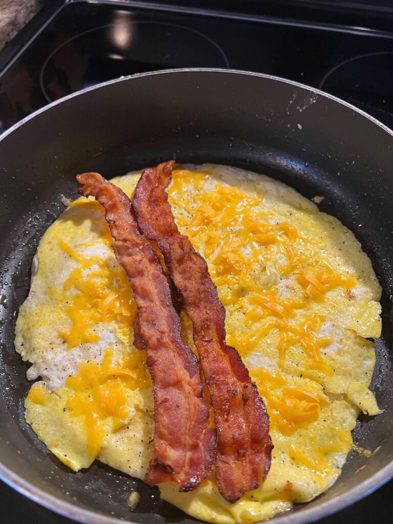 bacon and cheese on eggs on a tortilla in a pan