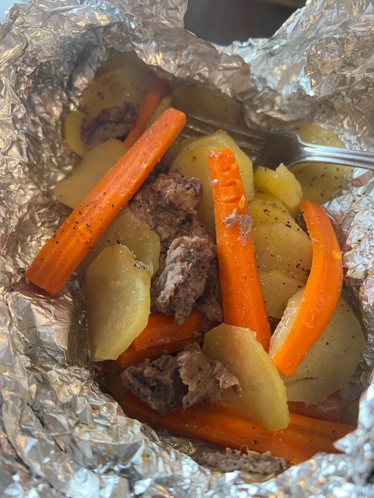 cooked hobo dinner packet in foil with hamburger, carrots and potatoes 