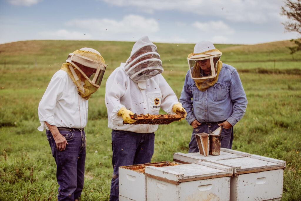 three men one man holding a beehive out in the field