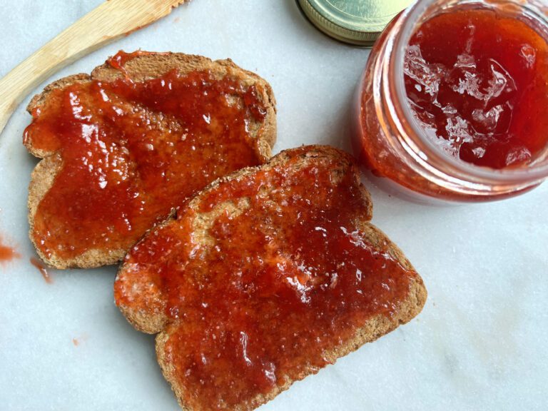 two slices of toast with strawberry apricot homemade jam with a jar of jam