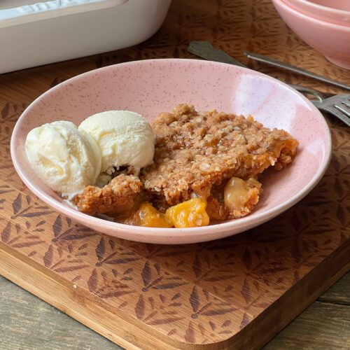 bowl of butterscotch peach crisp with a scoop of vanilla ice cream