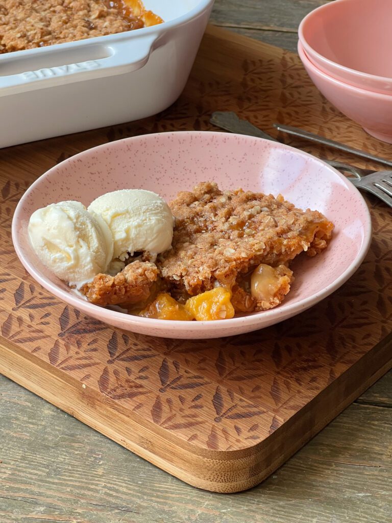 bowl of butterscotch peach crisp with a scoop of vanilla ice cream