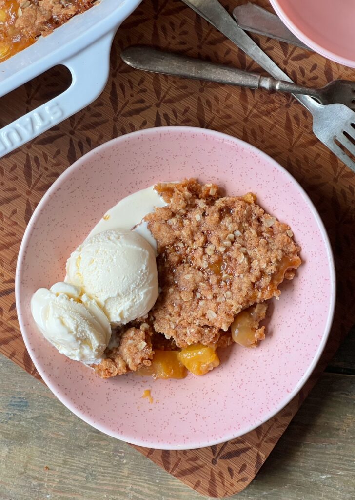 bowl of butterscotch peach crisp with a scoop of vanilla ice cream