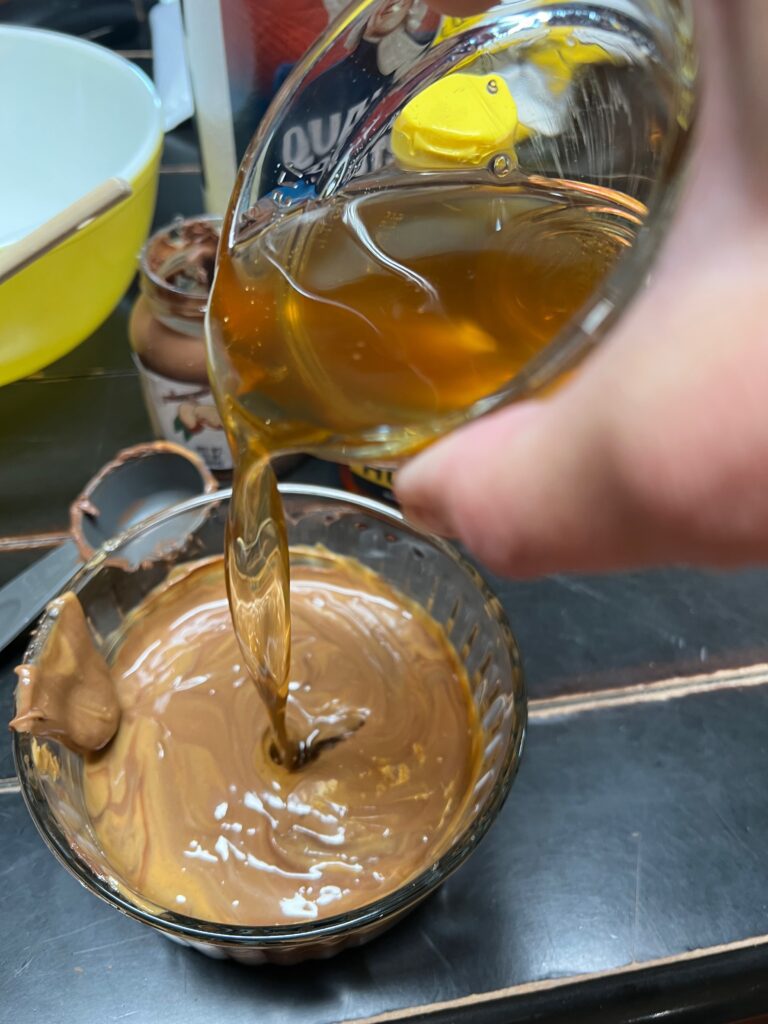 pouring honey into a mixture of peanut butter and cocoa almond spread 