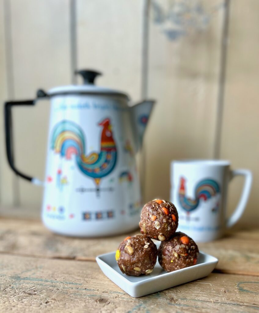 3 honey peanut butter and chocolate energy balls on a plate with a vintage coffee cup and carafe in the background