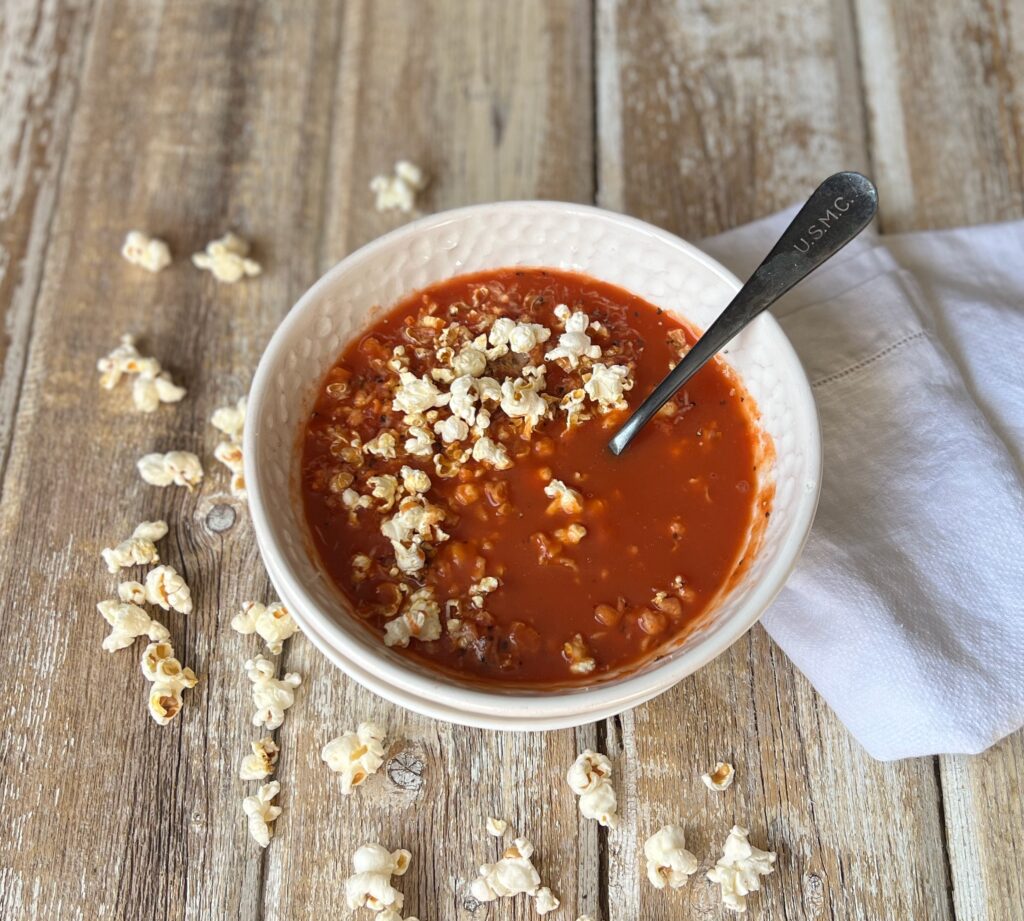 bowl of tomato soup topped with popcorn, parmesan cheese and black pepper 