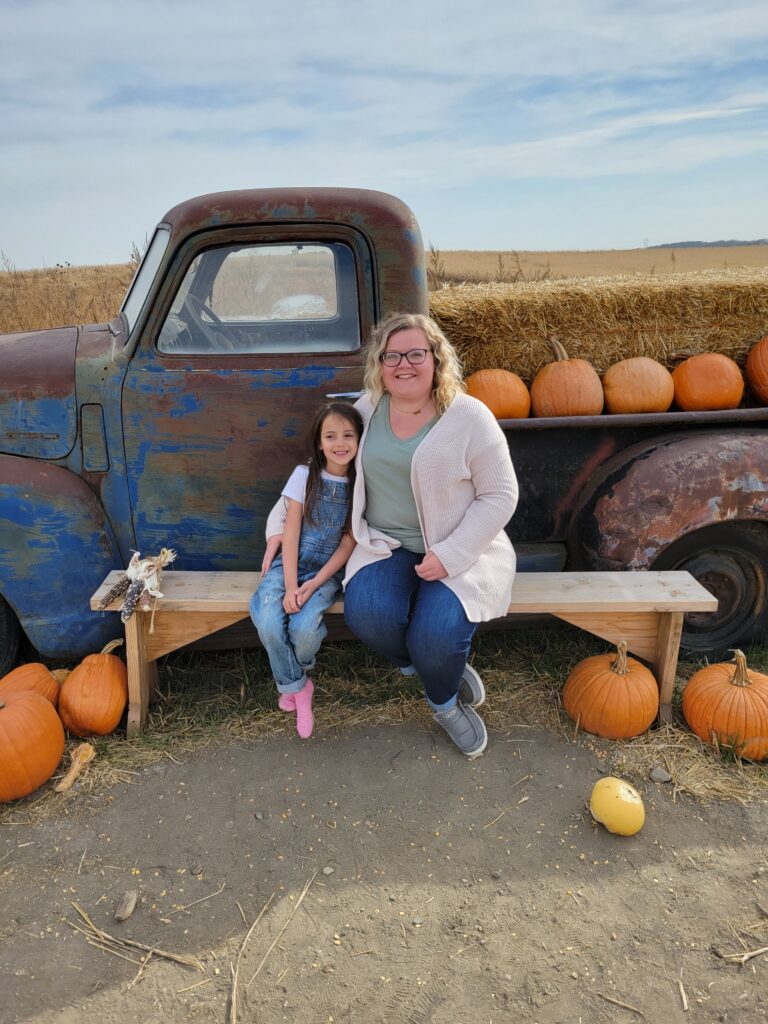 mom and daughter by a truck with pumpkins around it