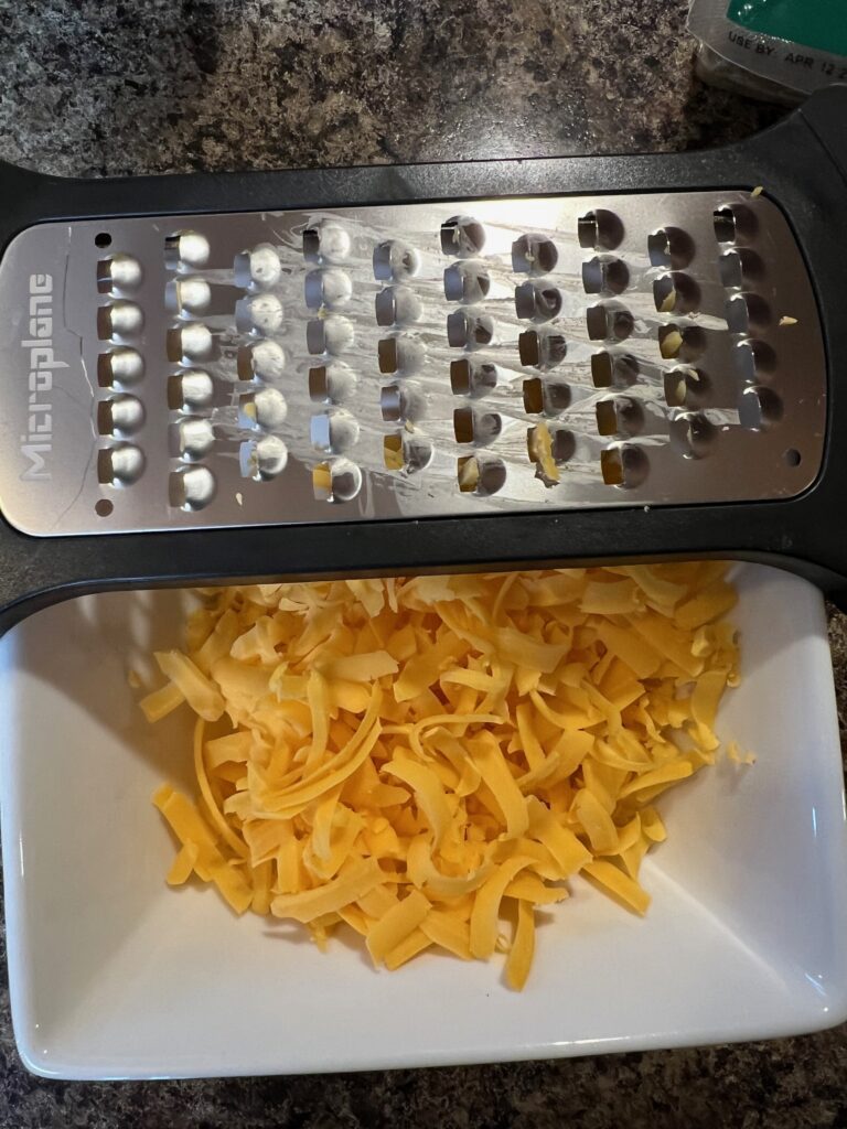 cheese grater and shredded cheddar cheese in a bowl