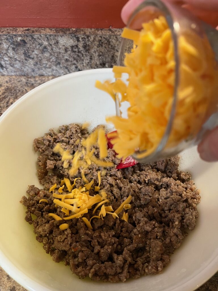 adding the shredded cheddar to the sausage in the bowl 