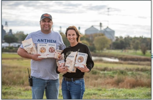 Taylor and Cassandra Sumption in a field holding Anthem Oats packages