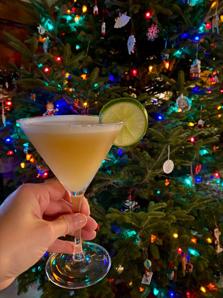 holding a cocktail in front of a lit Christmas tree 