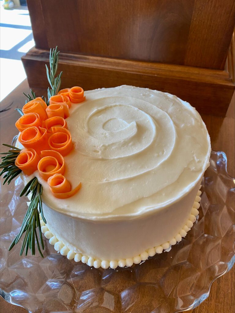 round carrot cake with white frosting and carrot peel decoration on top