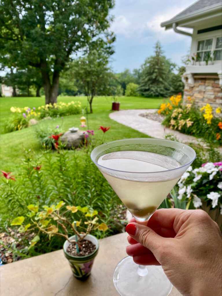 holding a cocktail on the porch with flowers in the background 