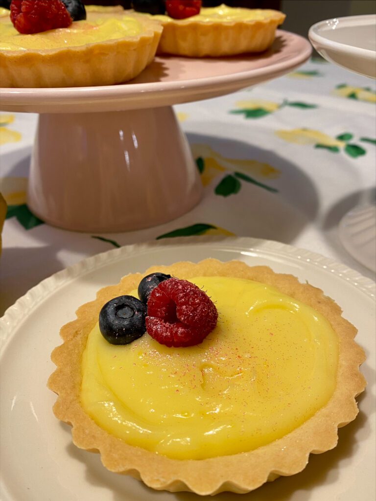 lemon tart on a plate with lemon tarts on a cake stand in the background