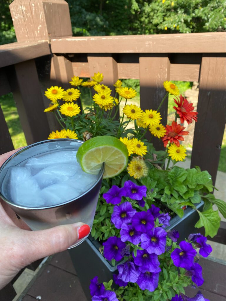 holding a cocktail outdoors with flowers in the background 