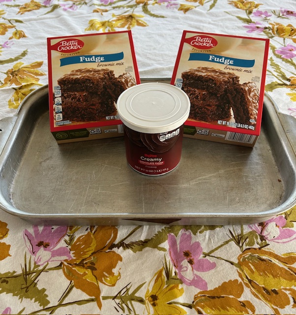 two boxes of brownie mix, a canister of chocolate frosting and a baking pan